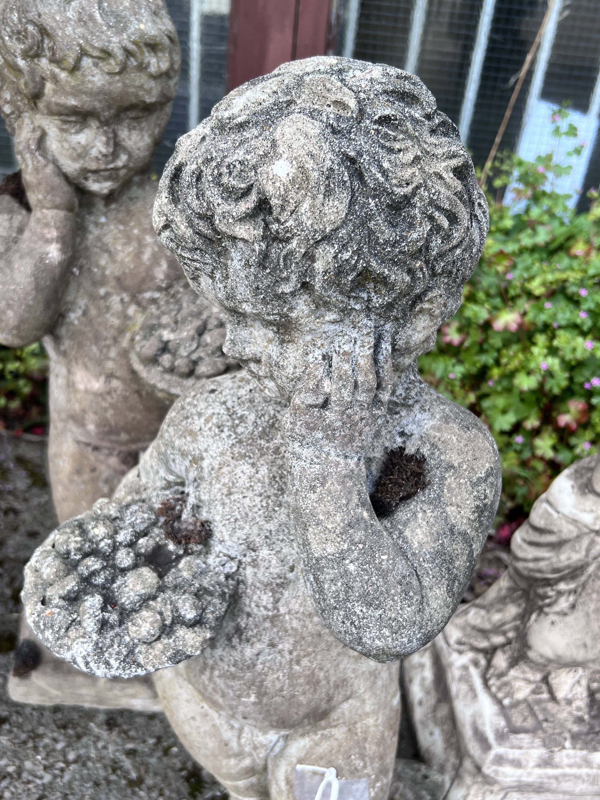 A pair of reconstituted stone garden ornaments, cherubs with fruit baskets, height 72cm